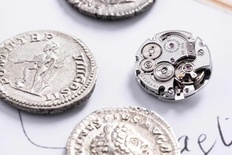 Vista macro del calibre Piccolissimo BVP100, desarrollado por Bvlgari en Le Sentier, comparado con auténticas monedas romanas del periodo 198–297 d.C