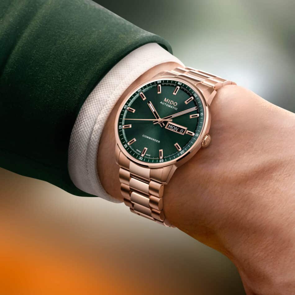 Commander Datoday Watches World Reloj MIDO Commander Datoday con carátula verde y caja en oro rosa sobre fondo oscuro en la muñeca de un caballero