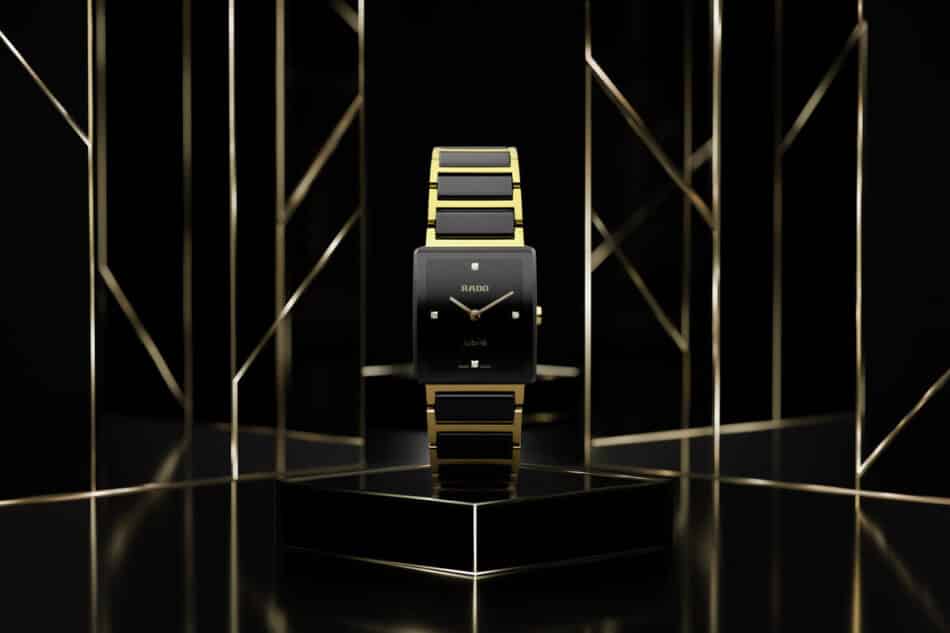 IntegralR20252702PRb Watches World Reloj de pulsera Rado Jubile en oro y negro sobre un pedestal negro en una sala de exposición oscura y geométrica con marcos metálicos que resalta su estilo lujoso