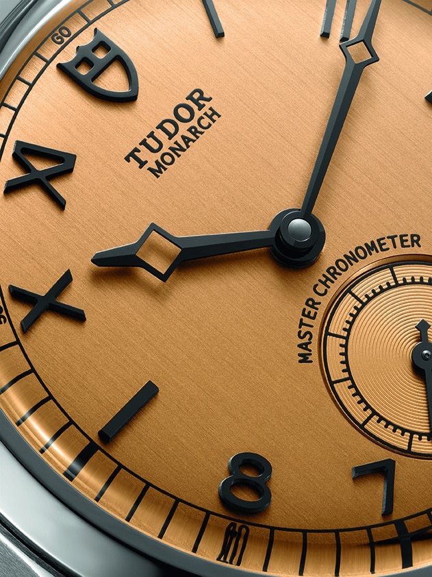 TUDOR Monarch con carátula color papiro y caja facetada de acero Watches World Primer plano de la carátula de un reloj Tudor Monarch Master Chronometer con agujas negras sobre una esfera en tono bronce y oro