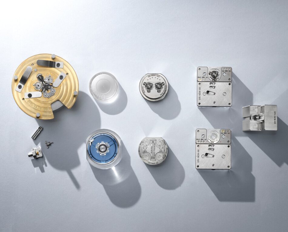 Ulysse Nardin Super Freak 1 Watches World Ulysse Nardin Super Freak primer doble tourbillon automático del mundo nuevo sistema de cardán of watch components laid out on a gray surface including a gold movement on the left and metal parts on the right