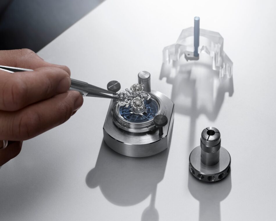 Ulysse Nardin Super Freak 3 Watches World Ulysse Nardin Super Freak primer doble tourbillon automático del mundo nuevo sistema de cardán Close up of a watch movement being adjusted with tweezers on a white work surface with shadows in the background showing gears and screws