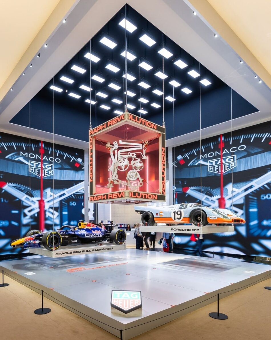 Watches and Wonders Geneva 2026 16 Watches World Watches and Wonders Geneva 2026 Race car exhibit with a suspended red glass engine case above two race cars and TAG Heuer branding in a showroom