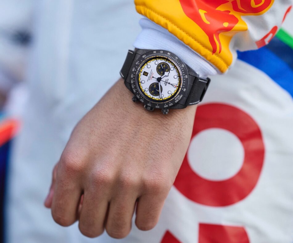 TUDOR Black Bay Chrono Carbon 26 Watches World Close up of a black chronograph watch on a person's wrist with a white dial and yellow accents.