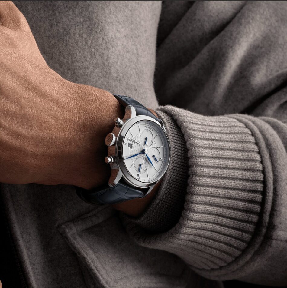 Baume Mercier Classima 10330LIFESTYLE Watches World Reloj de pulsera cronógrafo de acero inoxidable con agujas azules y correa de cuero oscuro expuesto en un una muñeca con suéter gris