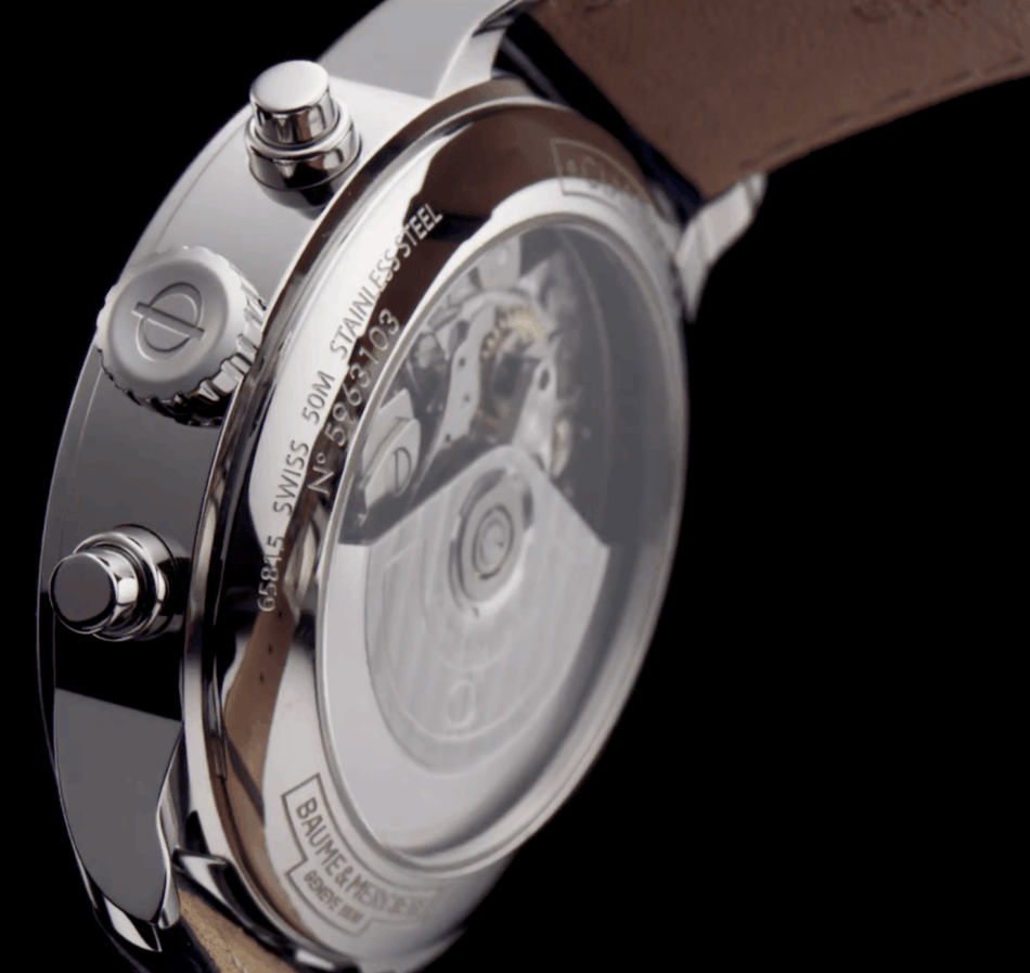 Baume Mercier Classima 10330VISTA TRASERA Watches World Vista trasera de un reloj de pulsera de acero inoxidable Baume Mersier Classima 10330 con caja transparente que deja ver el mecanismo mecánico engranajes rotor rubíes y correa de piel el logotipo de Baume Mercier es visible en el borde del rotor