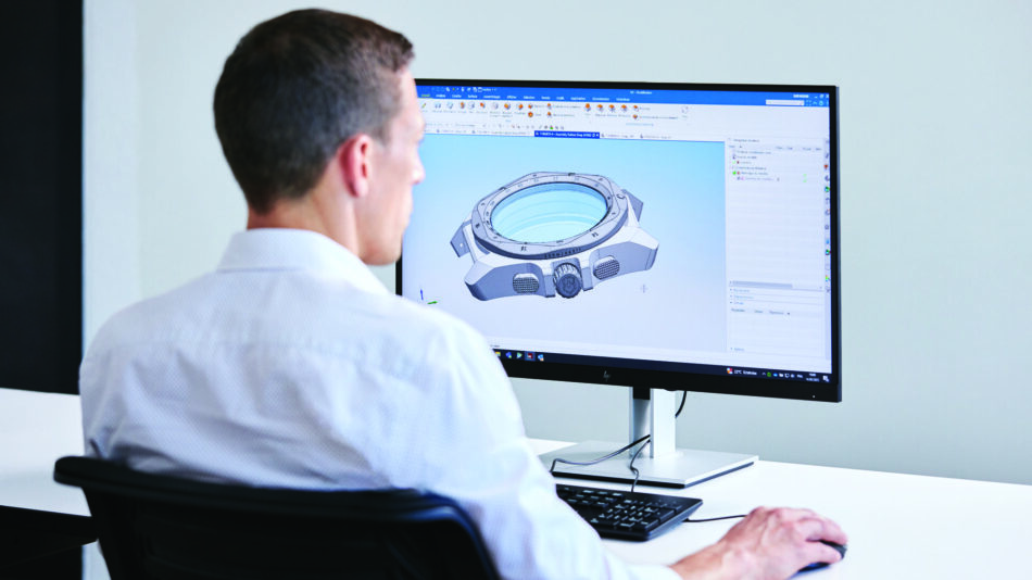 Centro de Competencia de Relojes de Victorinox 12 Watches World Man in a light shirt seated at a desk viewing a monitor displaying a 3D CAD model of a wristwatch