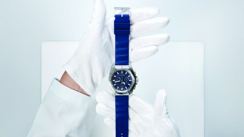 Centro de Competencia de Relojes de Victorinox 13 Watches World Close up of a silver wristwatch with a blue silicone strap held by a gloved hand in a clinical setting
