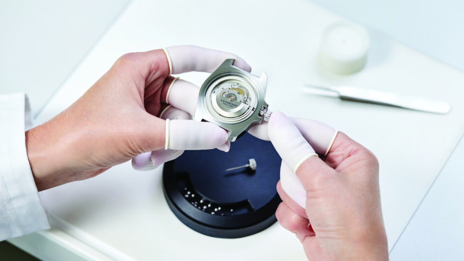 Centro de Competencia de Relojes de Victorinox 3 Watches World Centro de Competencia de Relojes de Victorinox Délemont Person wearing white gloves holding and opening a stainless steel watch to reveal its mechanical movement