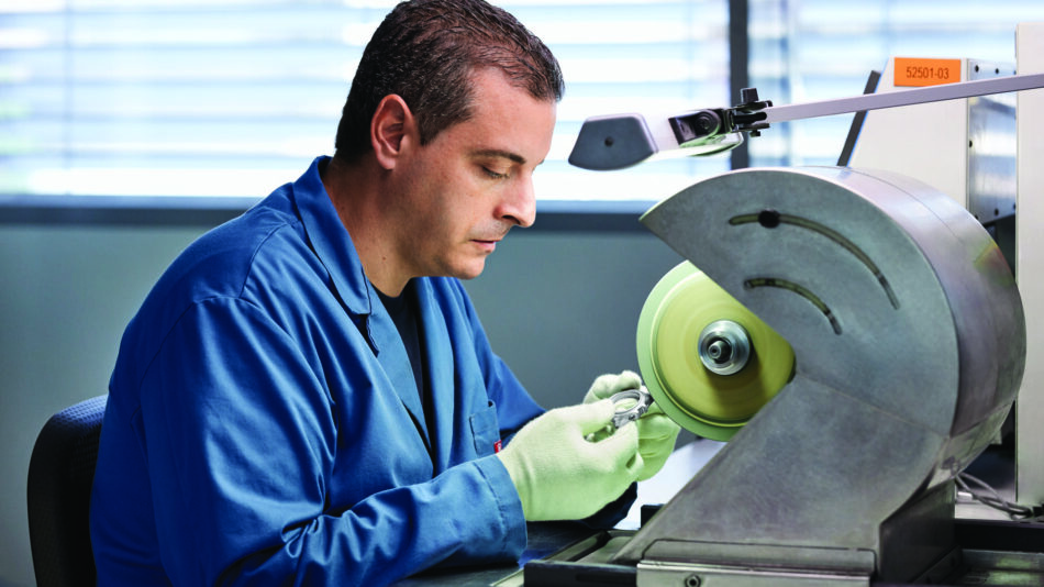Centro de Competencia de Relojes de Victorinox 6 Watches World Worker in blue coveralls operating a bench grinder with a spinning wheel in a workshop