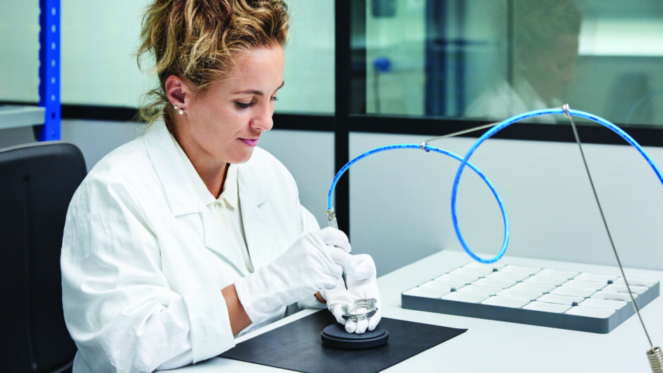 Centro de Competencia de Relojes de Victorinox 8 Watches World Scientist in a white lab coat sits at a lab bench examining a device with blue tubing in a modern laboratory with a keyboard nearby