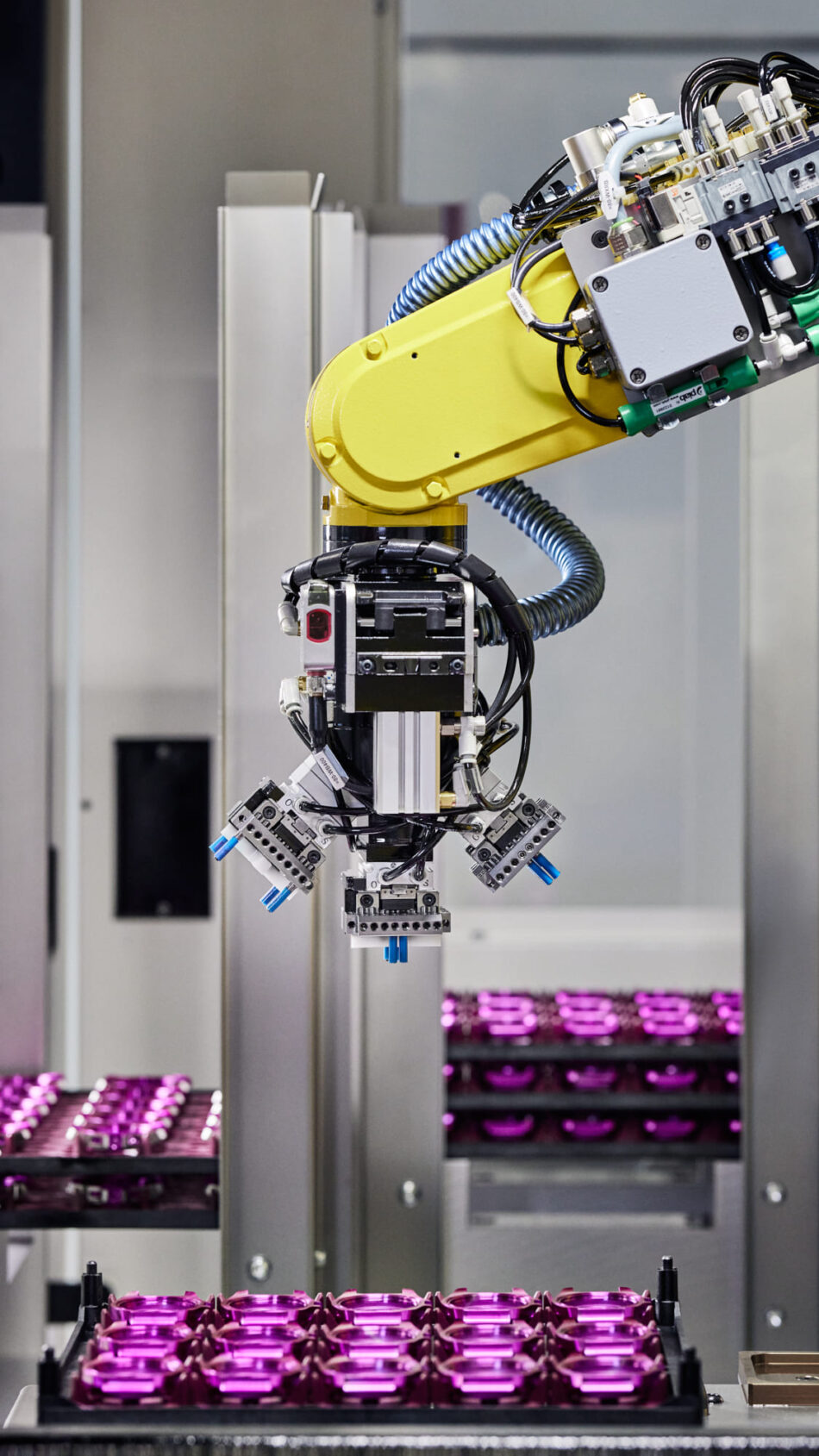 Centro de Competencia de Relojes de Victorinox 9 Watches World Centro de Competencia de Relojes de Victorinox Délemont Industrial robotic arm with yellow housing handling purple capsules on a production line in a lab like manufacturing setting