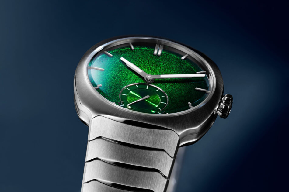 H Moser Streamliner Small Seconds Lime GreenCARATULA Watches World Close up of a silver wristwatch with a textured green dial metallic case and bracelet against a dark blue background showing large white hands and a small subdial near the bottom