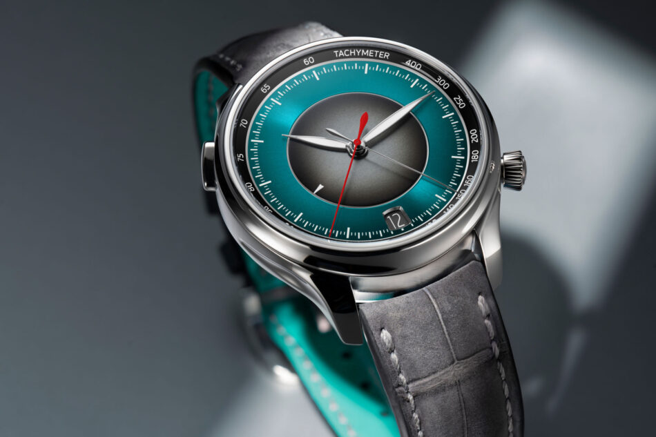 HMoser17301200EndeavourFlybackChronographDualTimeDateSTLifestyletopclose Watches World Close up of a silver wristwatch with a teal dial tachymeter bezel red second hand and a gray leather strap