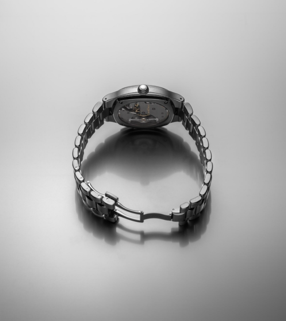 Laurent Ferrier Sport TravellerCOMPLETO ATRÁS Watches World Vista trasera del Sport Traveller de titanio con el fondo abierto que deja ver los engranajes internos colocado con un brazalete metálico circular colocado sobre una superficie brillante