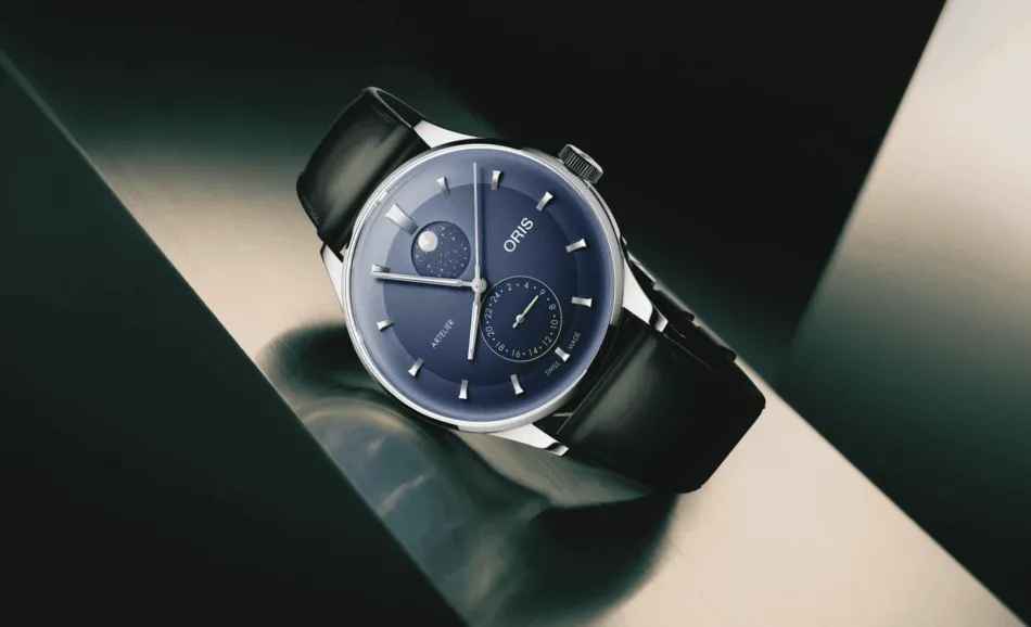 Close-up of a blue wristwatch with moon phase display and subdial, on a black leather strap.