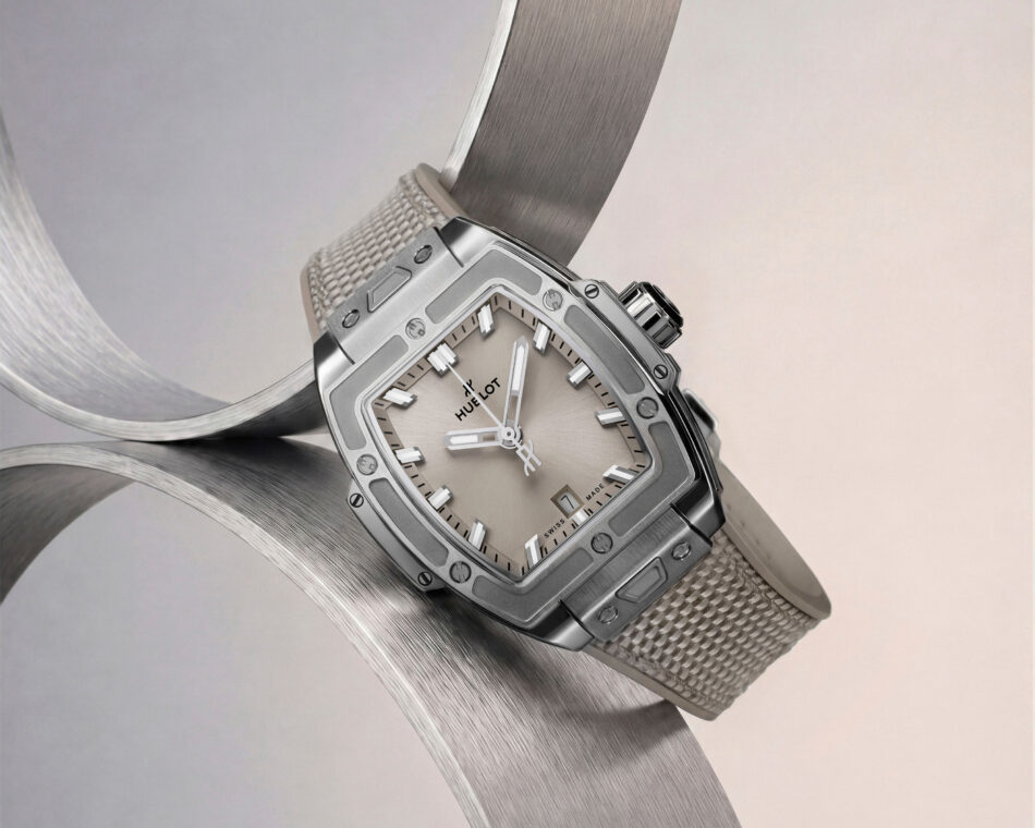 Spirit of Big Bang Essential Taupe 16 Watches World Primer plano de un reloj de pulsera Hublot cuadrado de acero inoxidable con correa metálica de malla y carátula gris sobre un fondo curvado