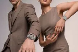 Dos elegantes modelos, vestidos con trajes de color topo, posan con relojes plateados a juego en la muñeca, poniendo de relieve los complementos para una sesión fotográfica de moda.