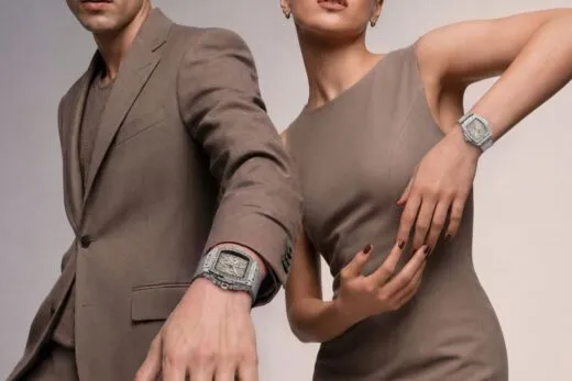 Dos elegantes modelos, vestidos con trajes de color topo, posan con relojes plateados a juego en la muñeca, poniendo de relieve los complementos para una sesión fotográfica de moda.