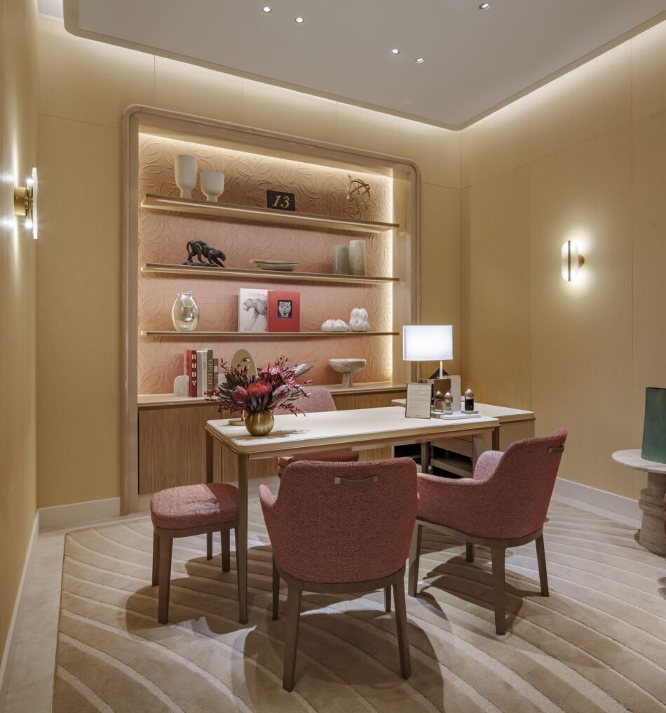 Boutique Cartier dentro de El Palacio de Hierro Monterrey 3 Watches World Boutique Cartier dentro de El Palacio de Hierro Monterrey A cozy showroom with a wooden table and pink upholstered chairs around it beige striped carpet and a wall shelf of decor items behind it
