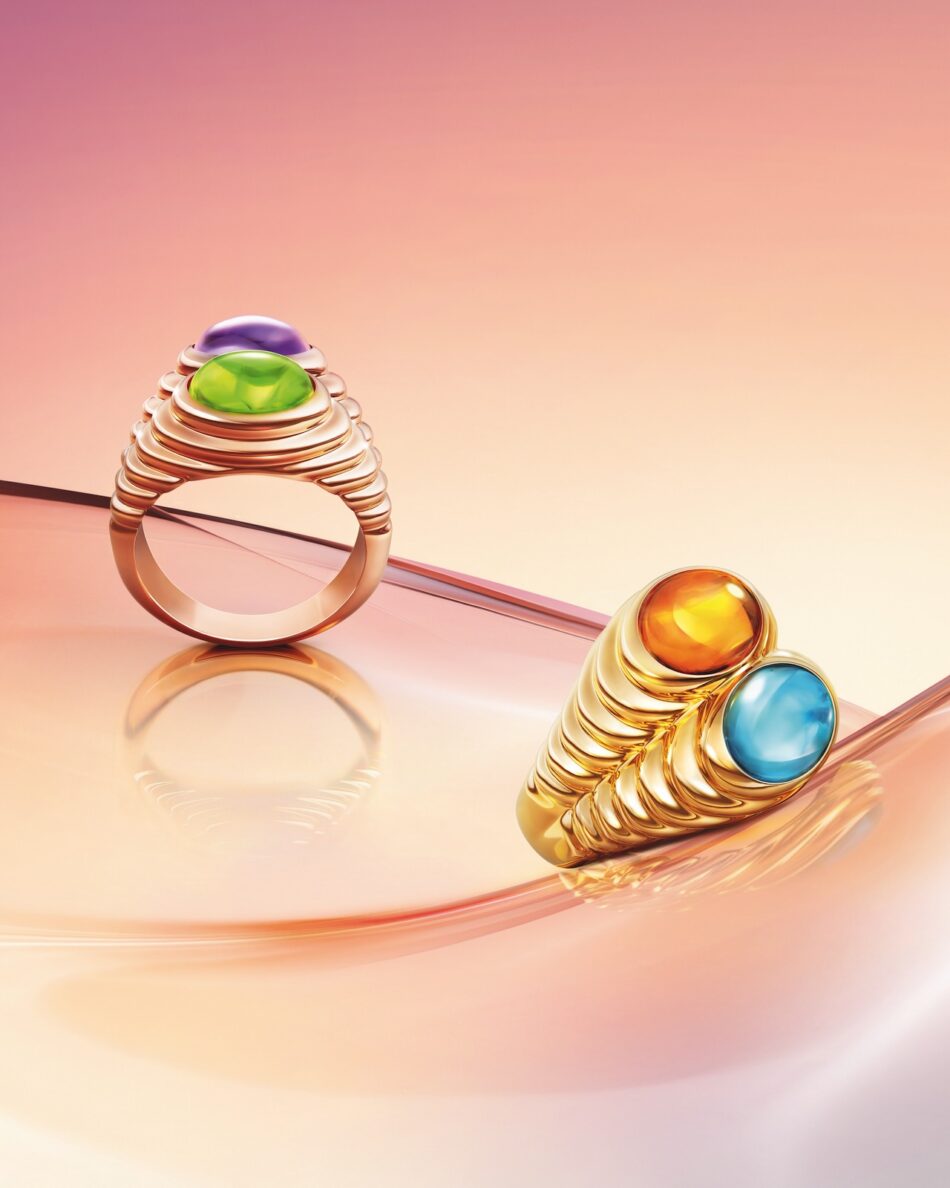 COMPANELLI copy Watches World Anillos de oro con bandas estriadas y piedras cabujón engastadas en bisel en tonos verdes y morados expuestos sobre una superficie rosa reflectante