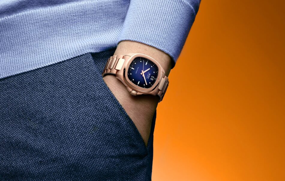 MIDO M0495263304100Multifort TV Big DatePR09 2 Watches World MIDO M0495263304100 Multifort TV Big Date PR09 2 Rose gold wristwatch on a wrist with a blue sweater and denim jeans orange gradient background product shot