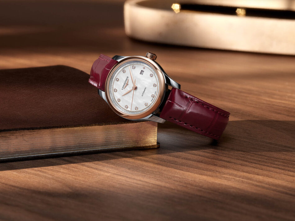 Longines reinventa la Master Collection con nuevos tamaños y carátulas texturizadas Watches World Watch with rose gold bezel white mother of pearl dial diamond hour markers and burgundy leather strap on a wooden surface