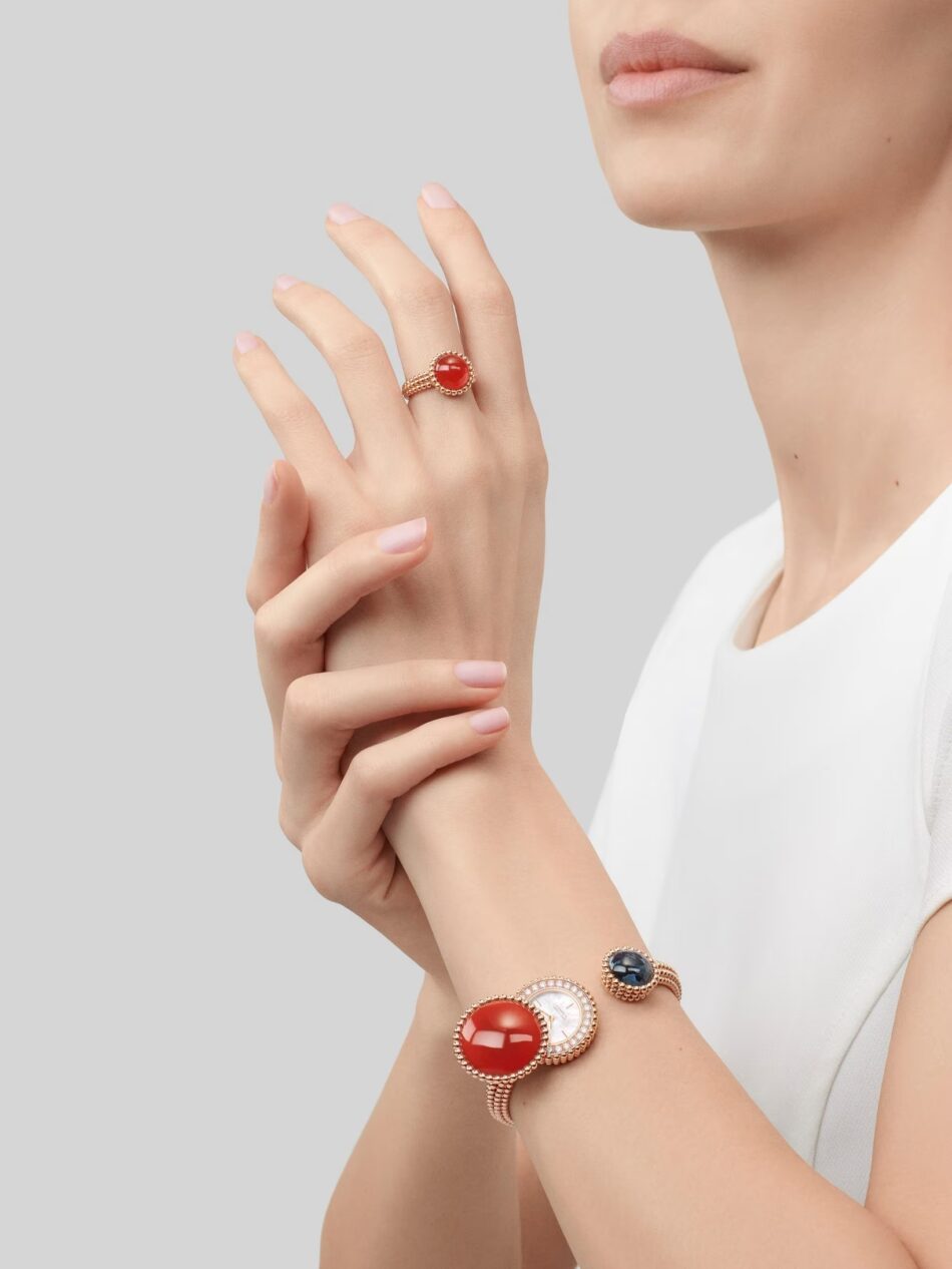 Relojes Perlée cuando la joyería y la relojería se encuentran en Van Cleef Arpels Watches World Mano de mujer con una pulsera de oro en la que destaca un gran anillo con un cabujón rojo sobre un fondo gris pálido