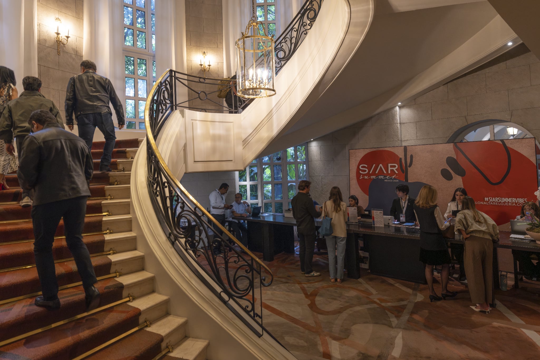 SIAR SUMMER 12 Watches World SIAR SUMMER Hotel lobby with a large curved staircase chandeliers and a registration desk where people are checking in at an event