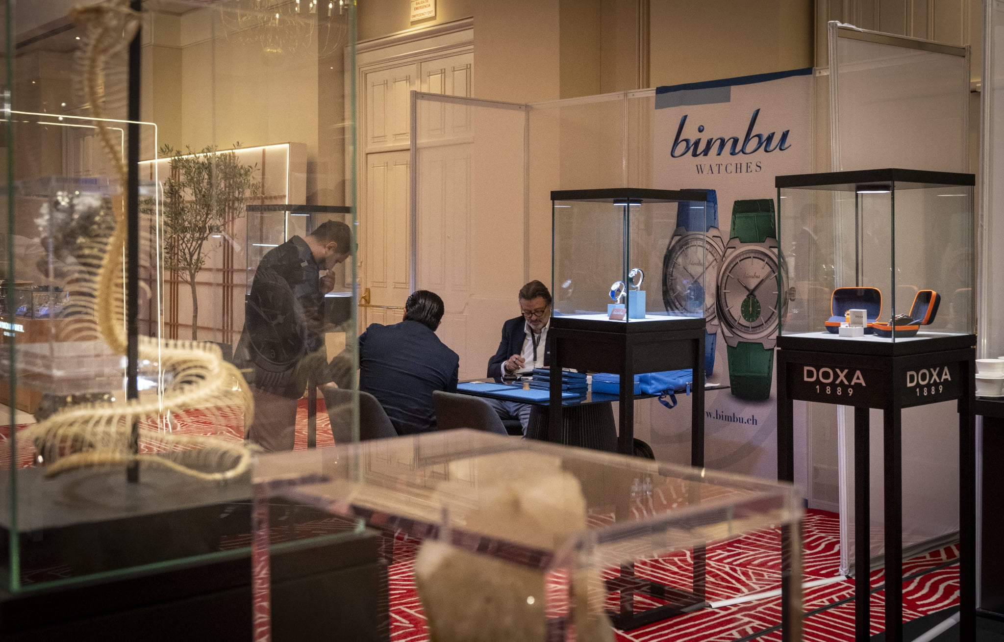 SIAR SUMMER 13 Watches World SIAR SUMMER Watch booth for bimbu Watches at an exhibition with glass display cases and two men sitting at a table reviewing materials
