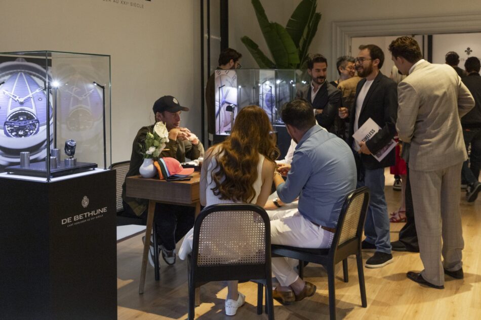 SIAR SUMMER 8 Watches World SIAR SUMMER Group of people at a watch showroomevent seated around a table with flower decor while glass display cases of watches tower nearby and a De Bethune podium is visible