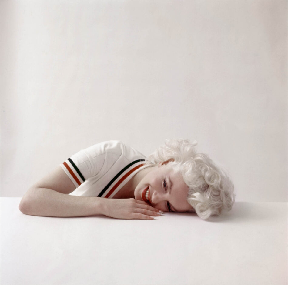 Marilyn Monroe y Blancpain la historia detrás de un legendario reloj joya Watches World Persona sonriente con el pelo rubio platino tumbada sobre una superficie blanca con la cabeza apoyada en los brazos cruzados vestida con una camisa blanca a rayas rojas y negras