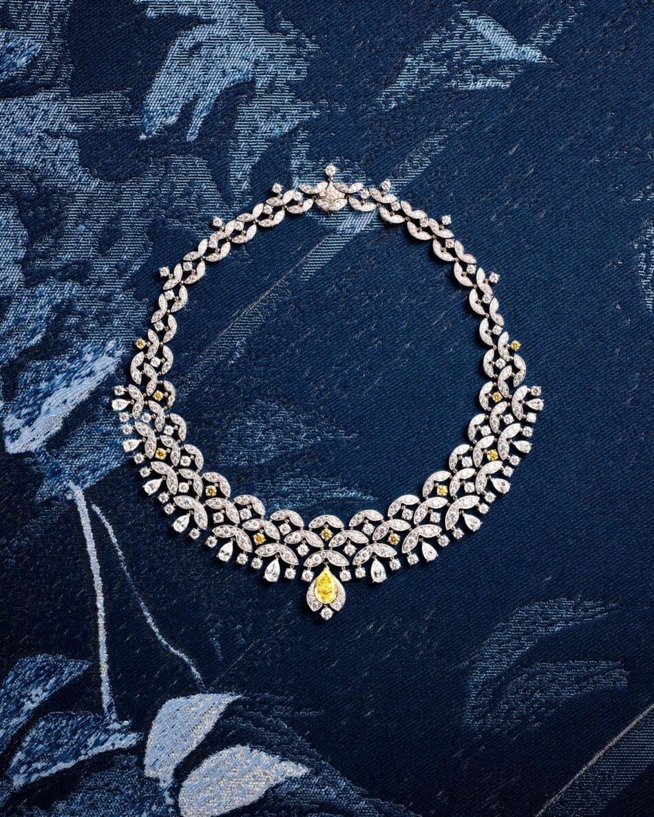 276606phAntonio Barrella4x5e Watches World Diamond necklace laid on dark denim fabric featuring alternating leaf shaped links and yellow gems at intervals