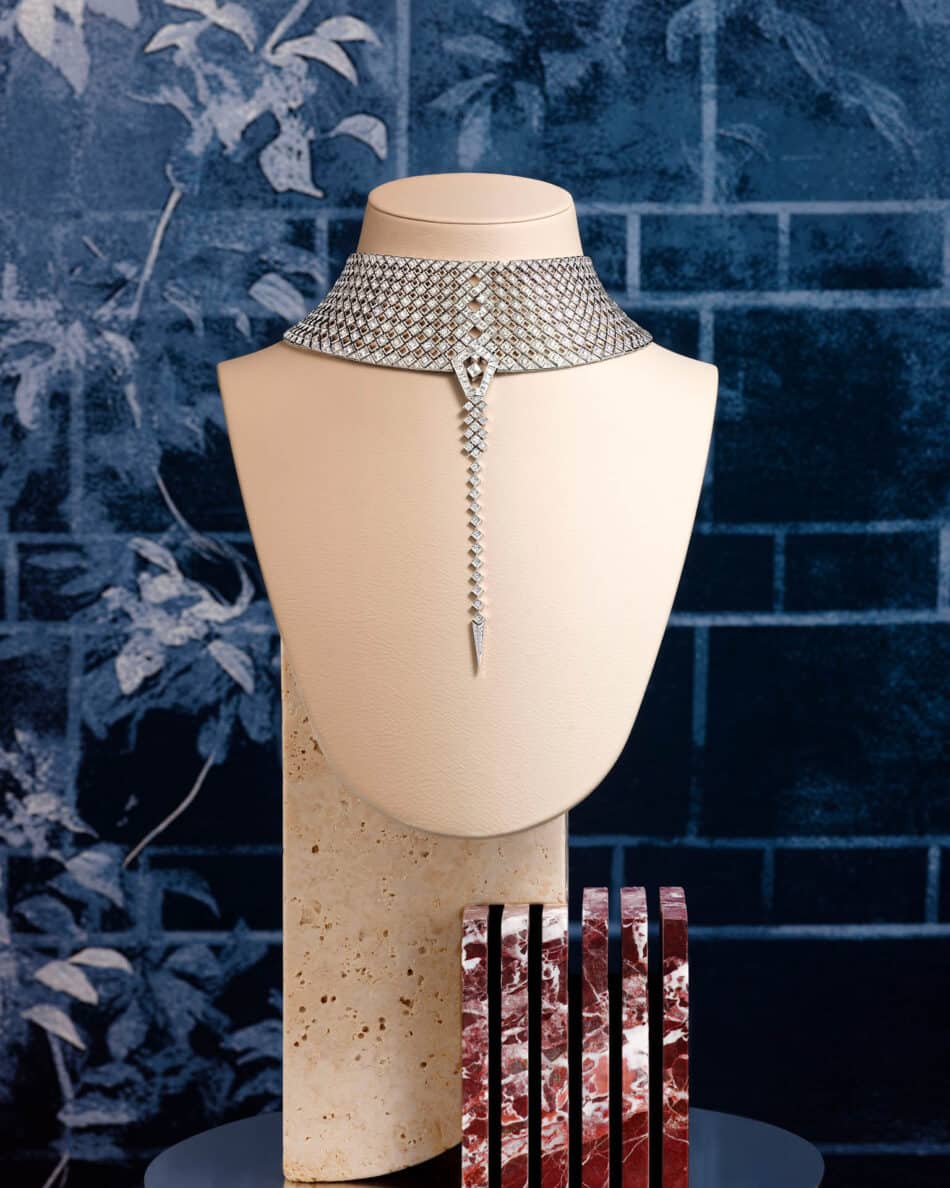 276610001phAntonio Barrella4x5 Watches World Diamond choker necklace with a long pendant displayed on a beige mannequin bust against a blue textured backdrop