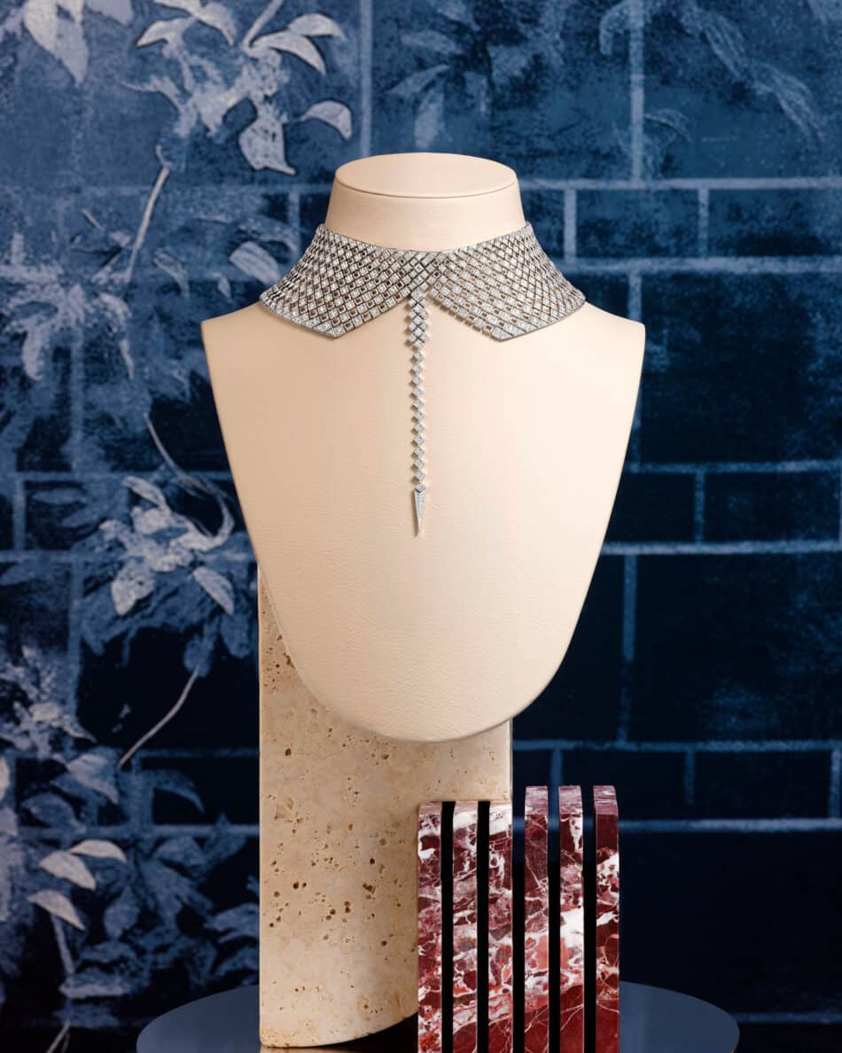 276610002phAntonio Barrella4x5 Watches World Diamond encrusted collar necklace on a cream display bust with a long diamond drop in the center against a blue backdrop