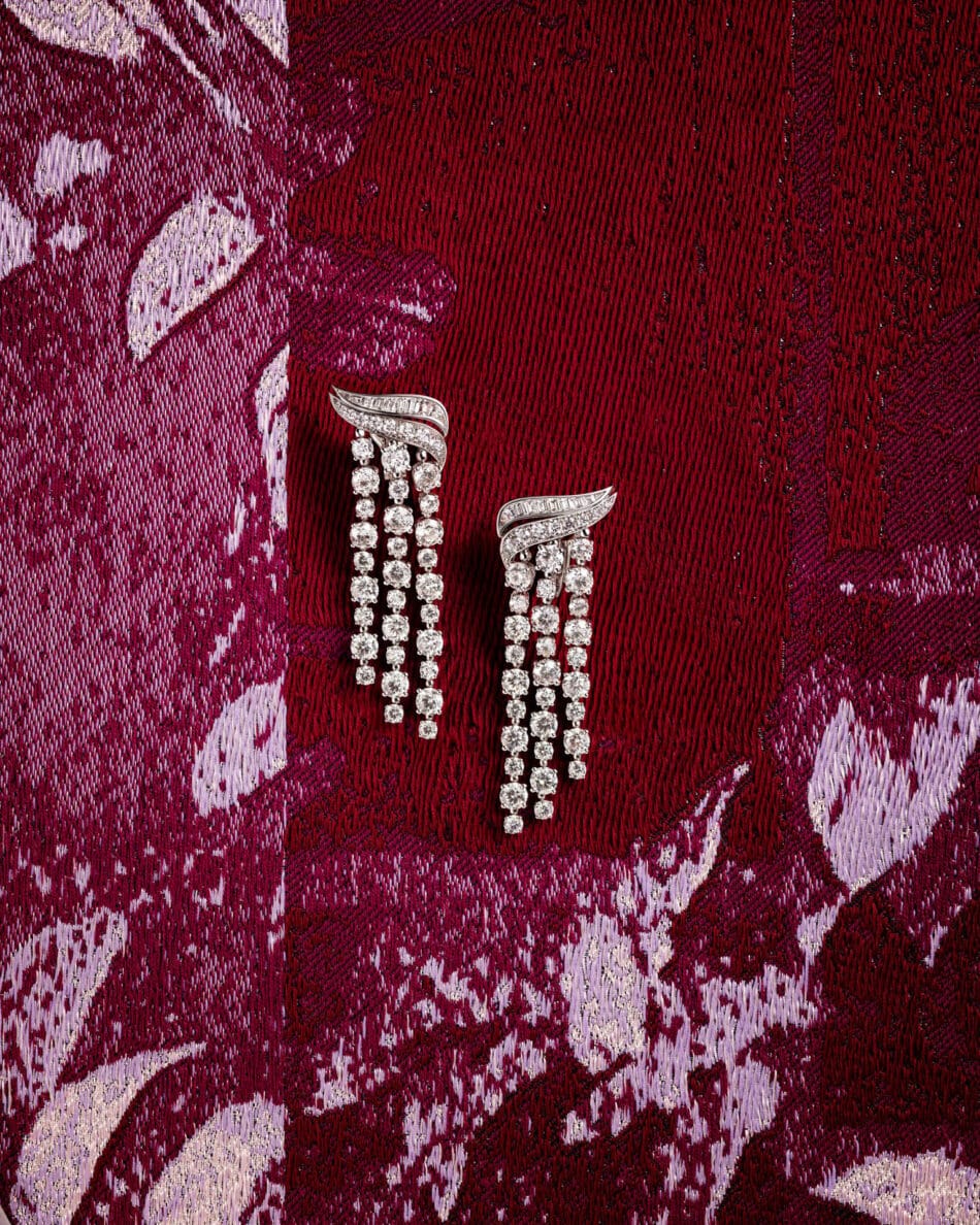276727phAntonio Barrella4x5 Watches World Diamond chandelier earrings with a curved silver top and three hanging strands of diamonds on burgundy fabric