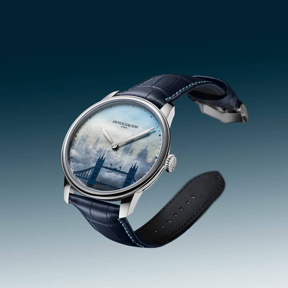 Stacked from 12 images Method=B R=8S=4 Watches World Close up of a blue leather strap wristwatch angled diagonally against a gradient blue sky showing a light blue dial with Arnold Son branding