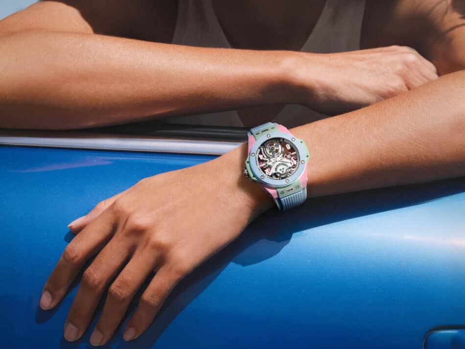 BIG BANG MULTI COLORED CERAMIC 44MM 2 Watches World Reloj esqueleto de colores en un antebrazo apoyado sobre la carrocería azul de un coche