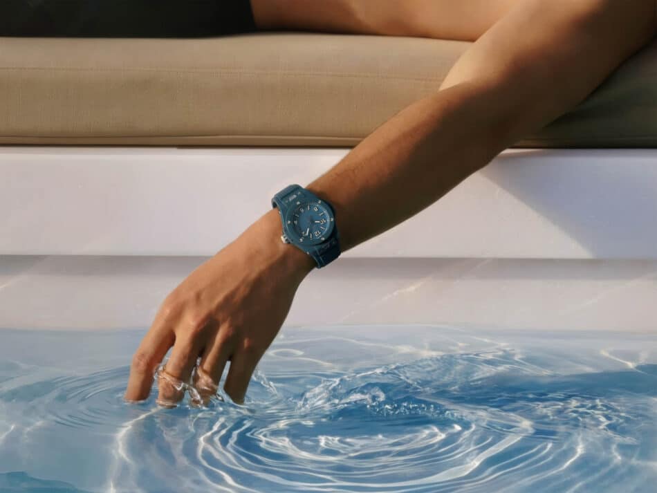 BIG BANG PETROL BLUE CERAMIC 2 Watches World Teal wristwatch on a forearm dipping a hand into a swimming pool near the edge water rippling around