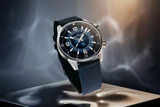 Jaeger-LeCoultre wristwatch with a blue dial and fabric strap, perched above a reflective surface on a dark, moody background.