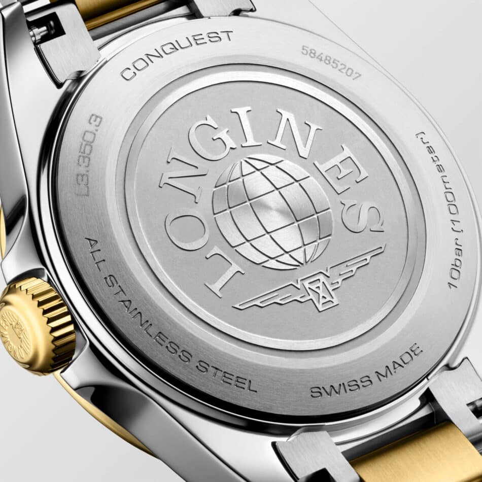 Longines renueva la colección Conquest con nuevos colores y cajas de 30 a 41 mm Watches World Primer plano del reverso de un reloj plateado con un emblema en forma de globo terráqueo y el grabado CONQUEST alrededor del borde en el que se aprecian una corona dorada y un detalle del brazalete bicolor