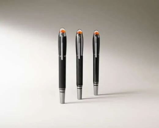 Montblanc StarWalker Extreme Three black pens with orange-tipped caps standing upright on a light beige background.