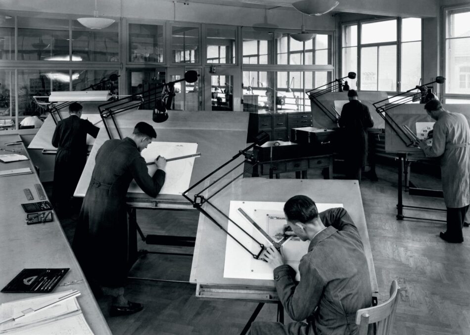 Oris Star y Dr Portmann 3 Watches World Oris Star y Dr Portmann Architects and draftsmen drawing technical plans at angled drafting tables under adjustable lamps in a bright studio in black and white
