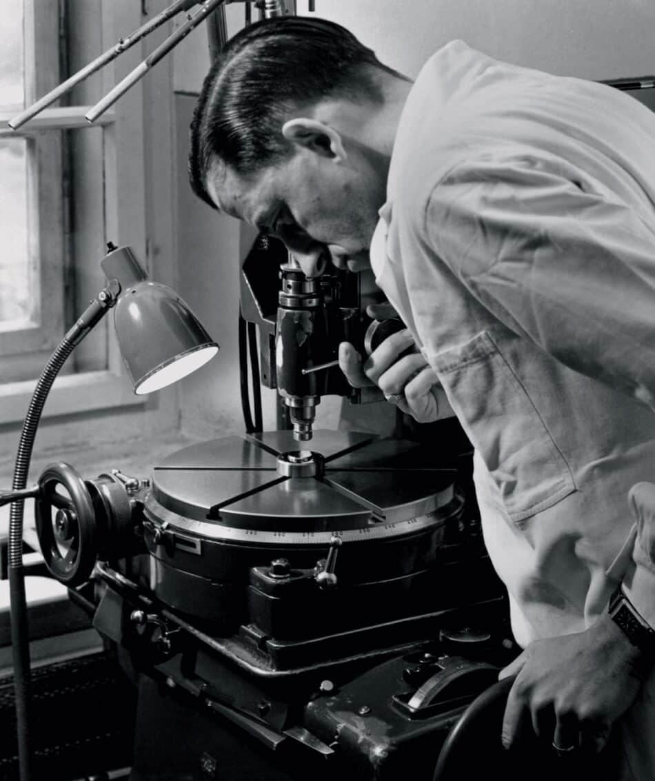Oris Star y Dr Portmann 5 Watches World Oris Star y Dr Portmann Black and white photo of a man in a lab coat leaning over a vintage precision instrument inspecting a central rotary device under a desk lamp