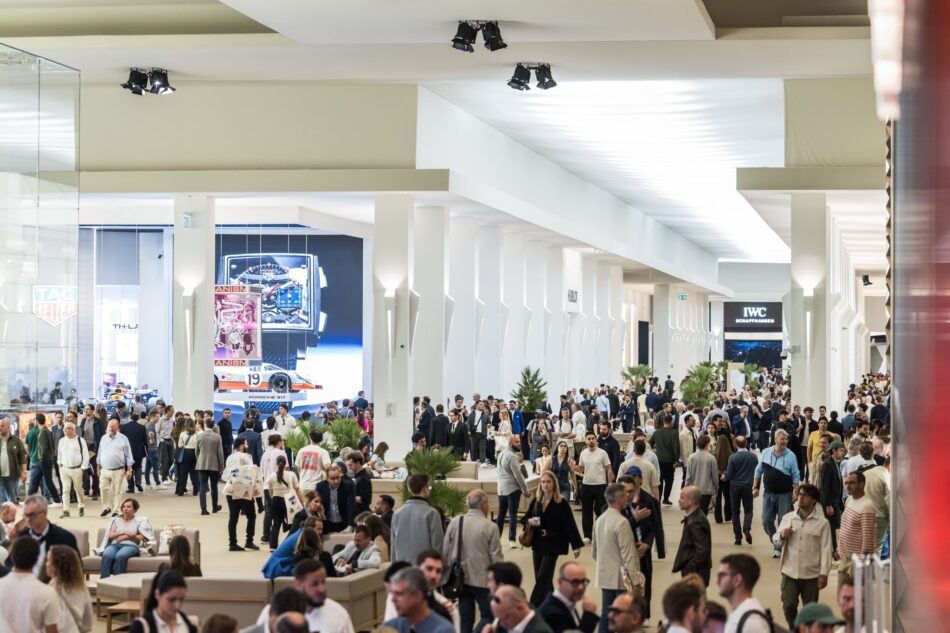 Watches and Wonders Geneva 4 Watches World Busy indoor trade show hall with a crowd white pillars and display booths car posters and watch brand signage in the background