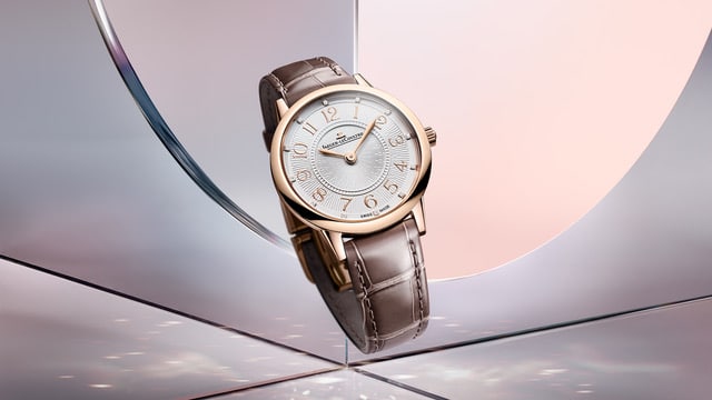 RendezVous HourMinute1 Watches World Reloj de pulsera de oro rosa con correa de piel marrón expuesto sobre una superficie reflectante que muestra una esfera blanca con números arábigos e índices en relieve