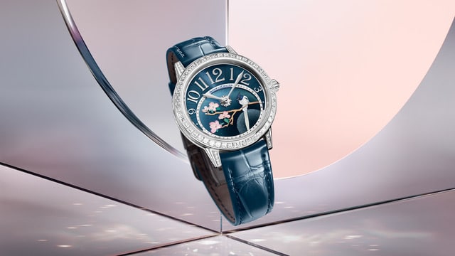 RendezVous Jewellery Night Day Watches World Lujoso reloj de piel azul con bisel engastado con diamantes y una esfera con motivos florales y de pájaros expuesto sobre superficies reflectantes