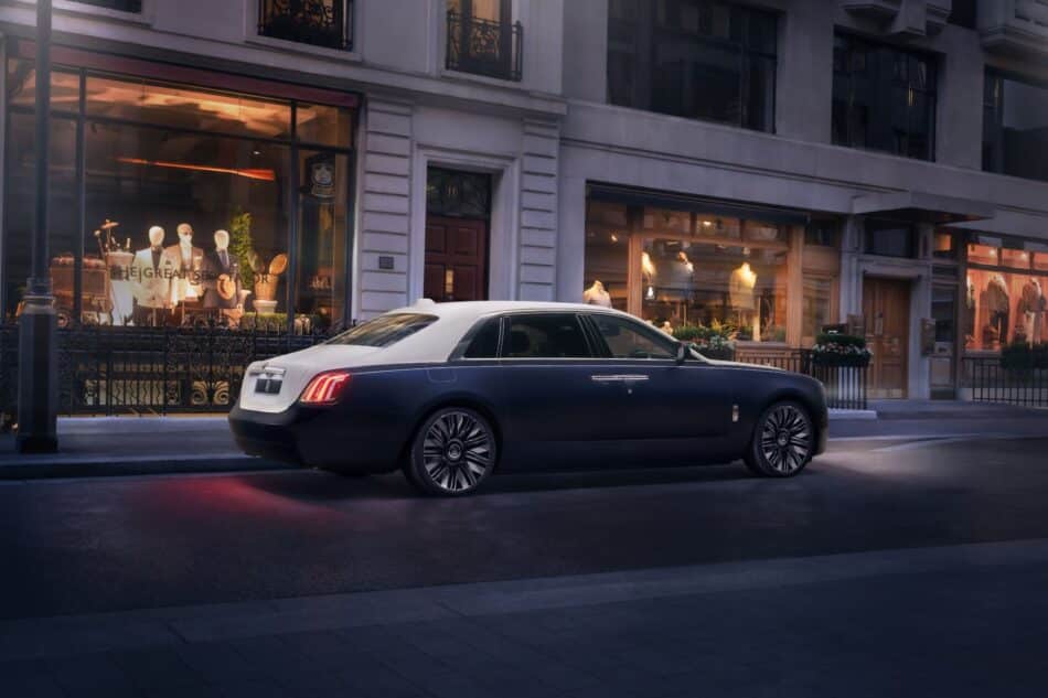 RollsRoyce Ghost Savile Row 6 Watches World Rolls Royce Ghost Savile Row Dark blue luxury sedan parked on a city street in front of a clothing store window display with mannequins wearing suits and hats visible inside the shop